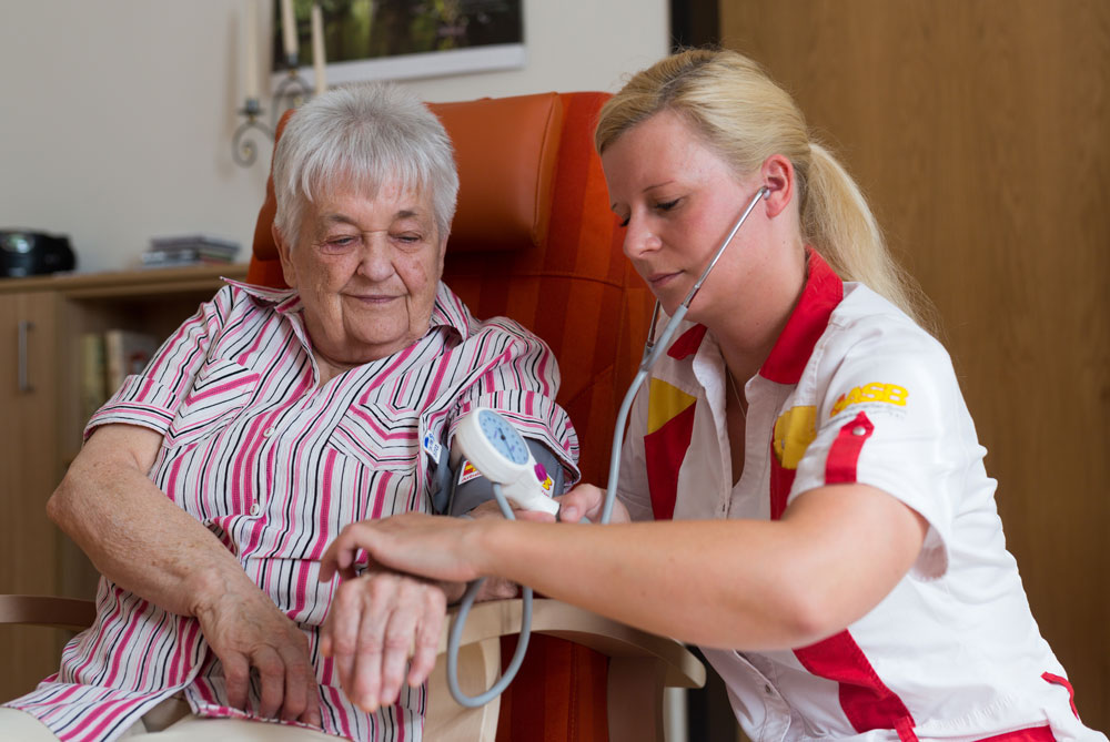 Mitarbeitende des ambulanten Pflegedienstes überprüft den Blutdruck einer Seniorin