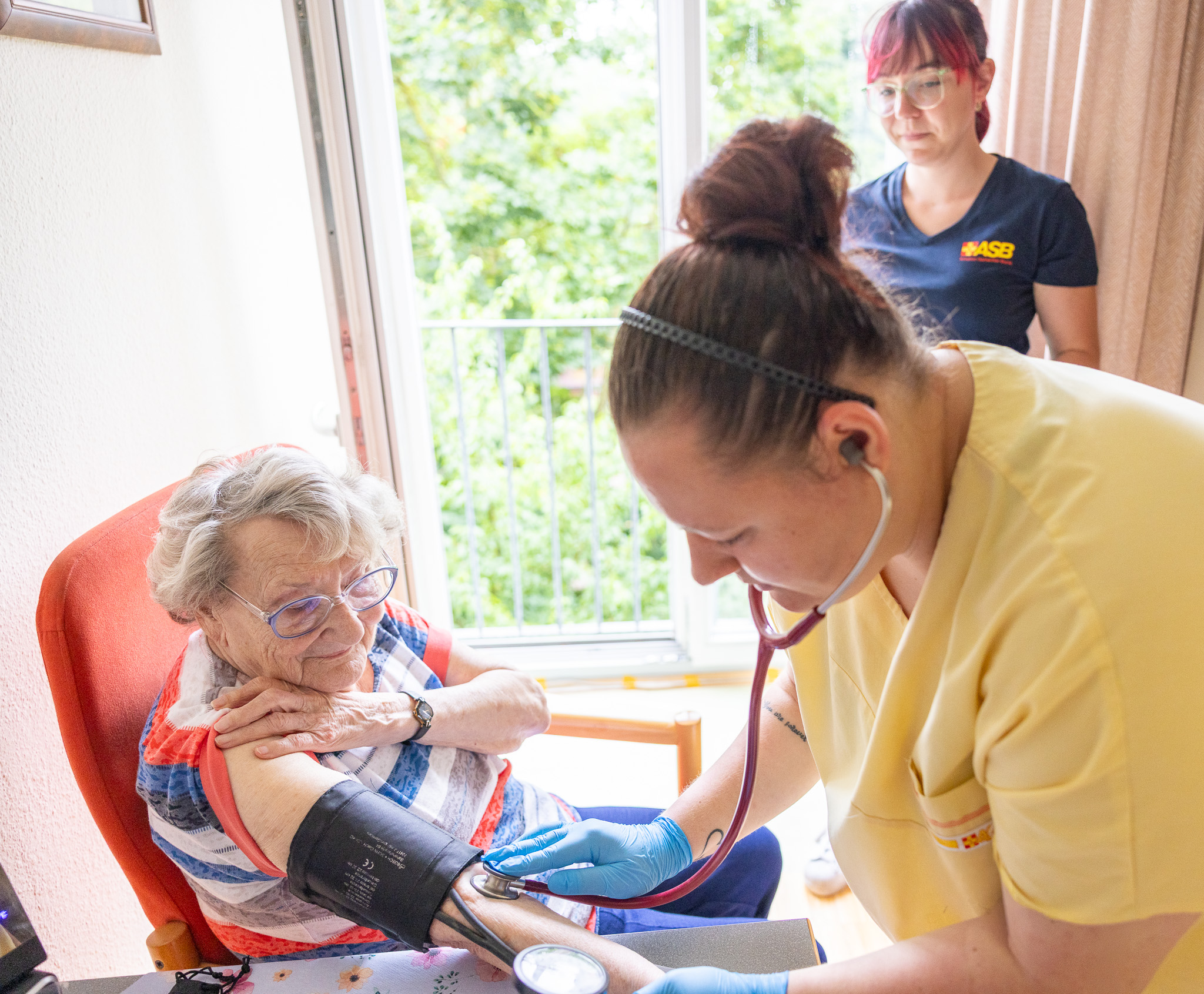 Einer Seniorin wird durch eine Pflegefachkraft in Ausbildung der Blutdruck gemessen. Die Schülerin legt gerade die Blutdruckmanschette an.